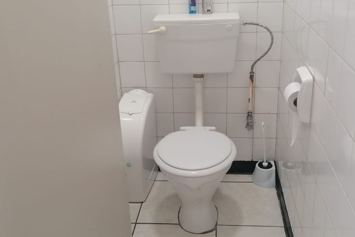 A compact commercial restroom featuring white wall and floor tiling, a standard toilet suite, and a wall-mounted toilet paper holder.