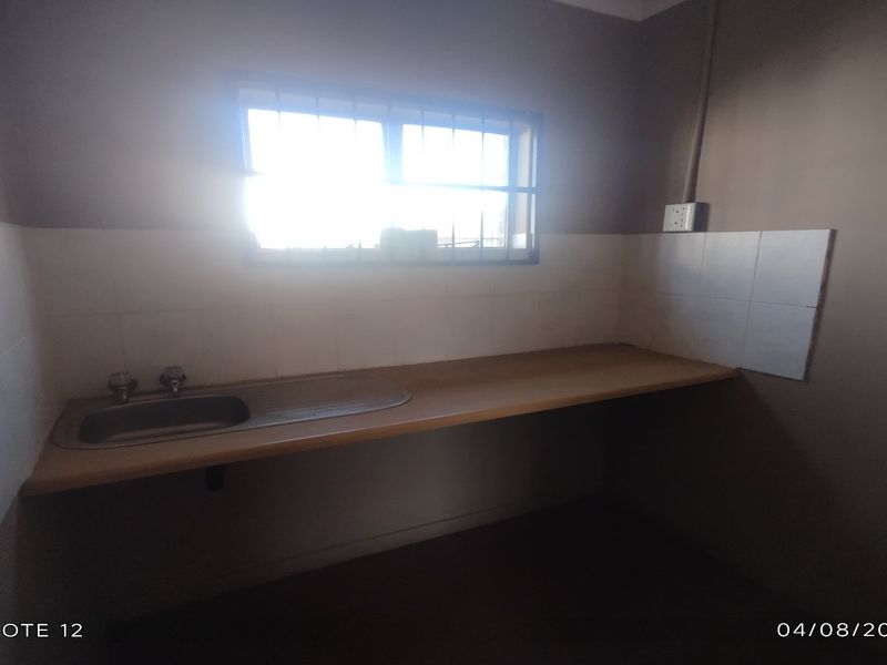 A functional scullery or utility area featuring a stainless steel sink, tiled splashback, and a long countertop, suitable for prep or wash-up tasks.