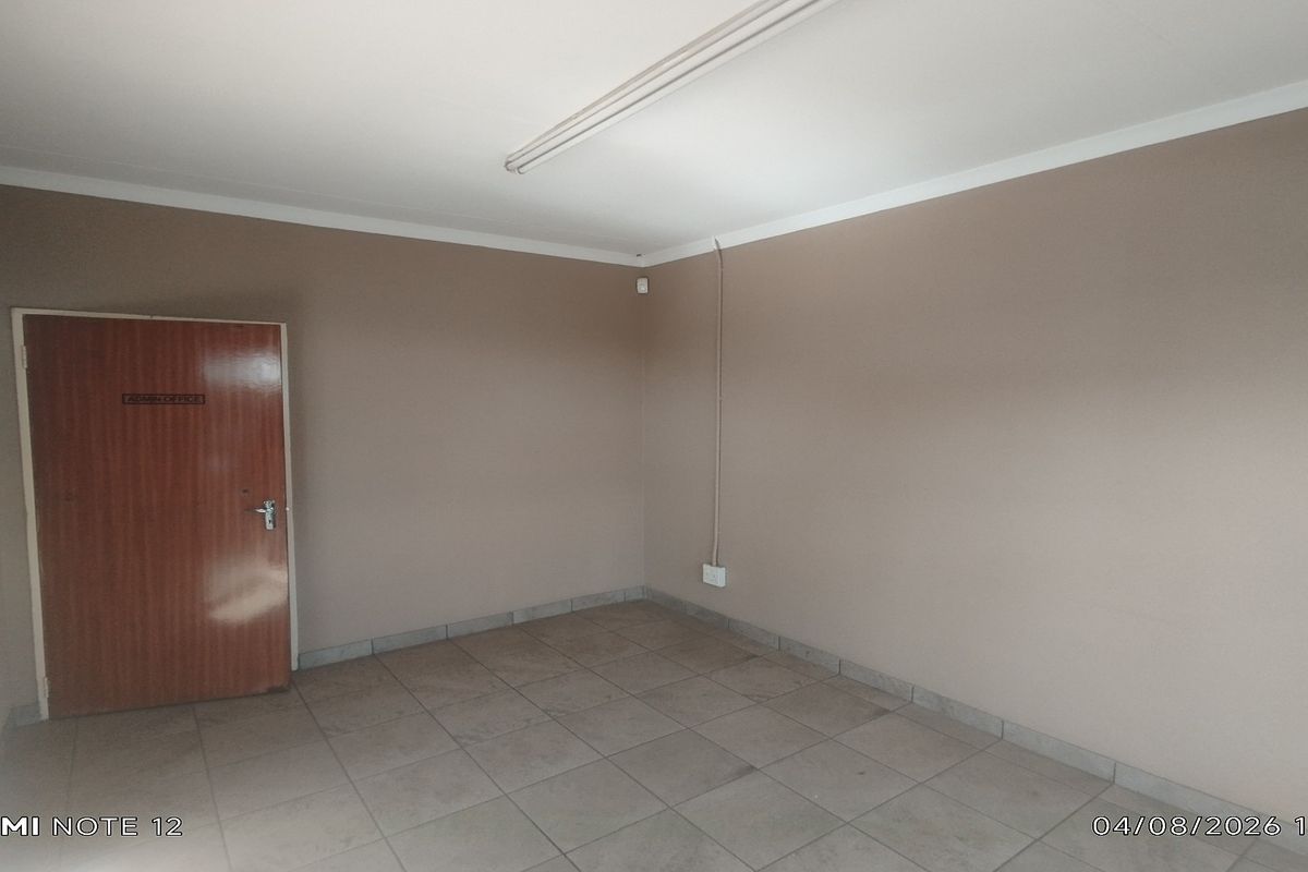 A vacant office space featuring neutral wall finishes, tiled flooring, and functional overhead lighting, suitable for a professional workspace.