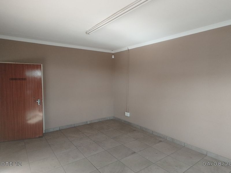 A vacant office space featuring neutral wall finishes, tiled flooring, and functional overhead lighting, suitable for a professional workspace.