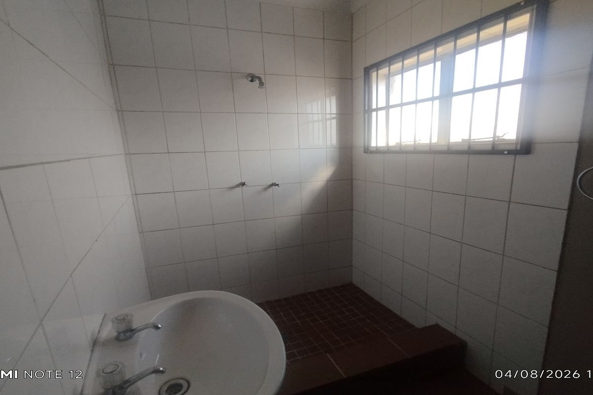 A basic bathroom featuring tiled walls and flooring, a pedestal basin, and a shower area with security bars on the window.