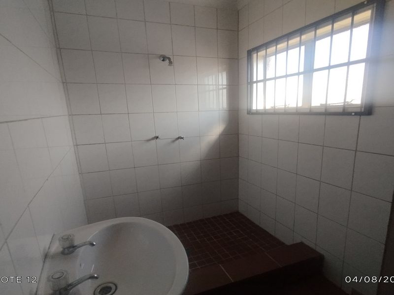 A basic bathroom featuring tiled walls and flooring, a pedestal basin, and a shower area with security bars on the window.