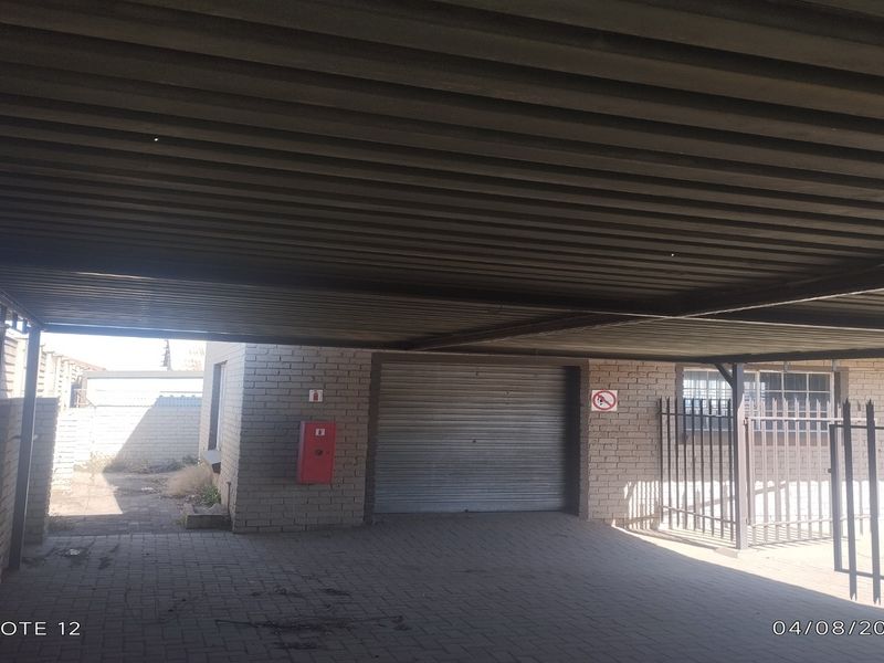 A covered industrial parking area featuring a corrugated metal roof, roller shutter door, and secure metal fencing.
