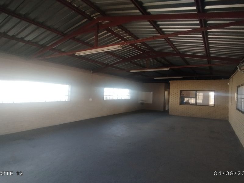 Spacious industrial utility area featuring exposed steel roof trusses, painted concrete flooring, and secure window fixtures, suitable for workshop or storage use.
