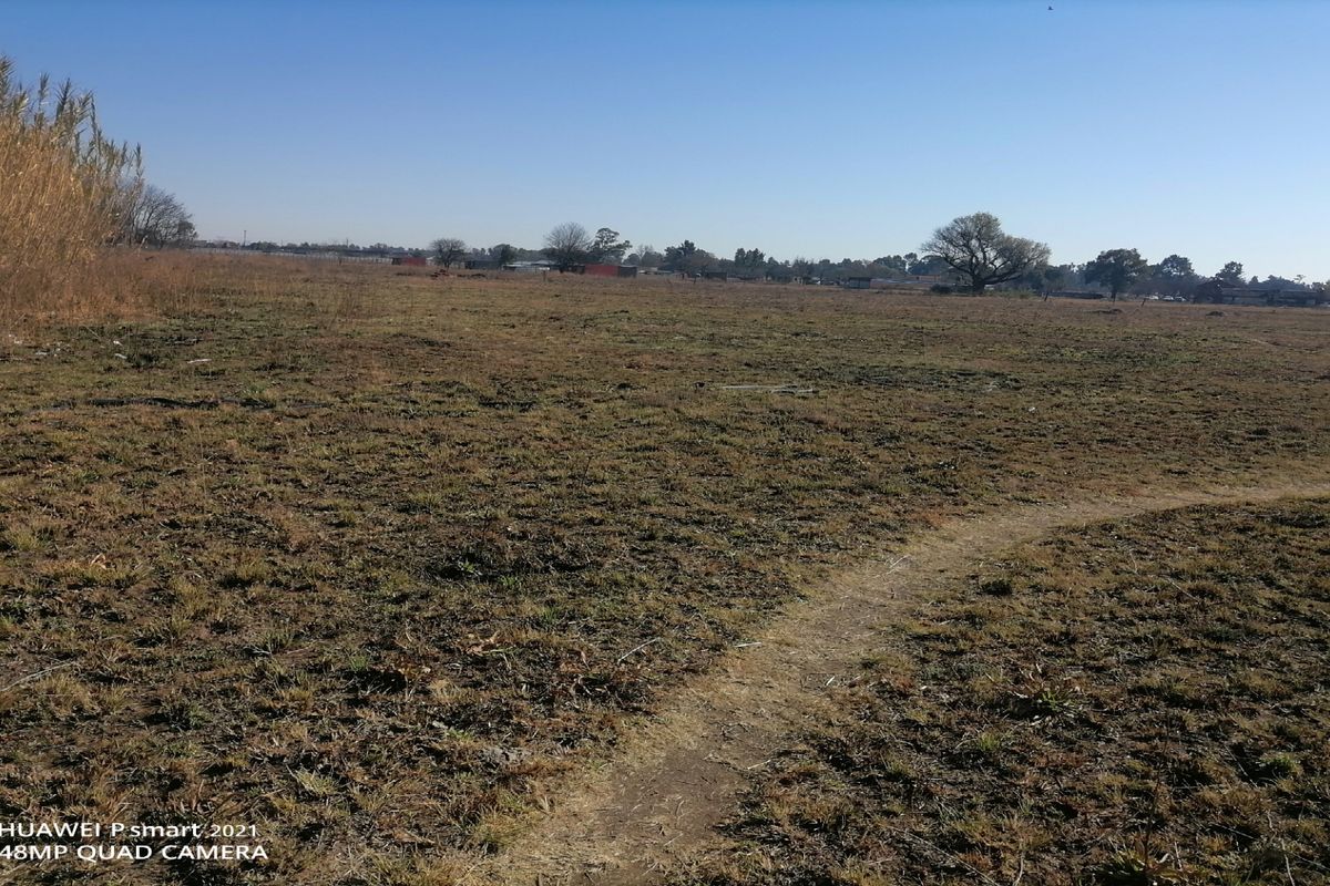 An expansive, undeveloped plot of land featuring natural grass cover and a dirt pathway, suitable for future development or agricultural use.