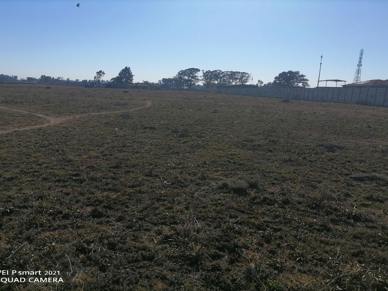 A large, undeveloped vacant plot of land featuring a perimeter wall and open grass area.