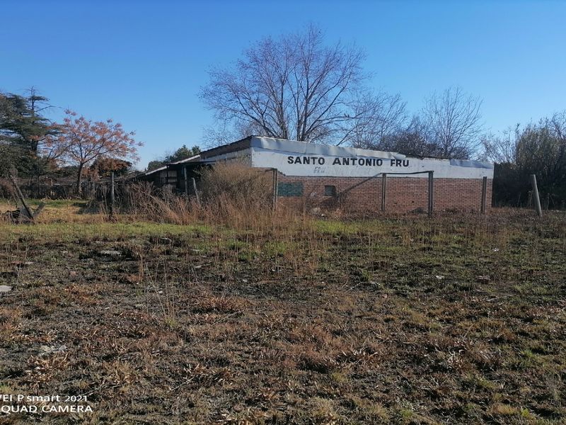 Exterior view of a commercial building structure showing significant wear and surrounding overgrown land.