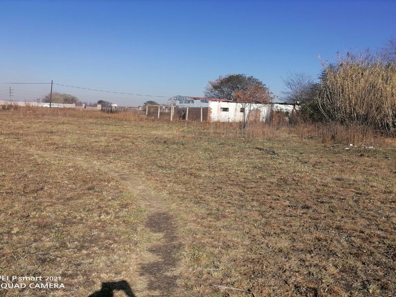 A wide-angle view of a large, undeveloped plot of land featuring dry grass, perimeter fencing, and a small, weathered outbuilding in the distance.