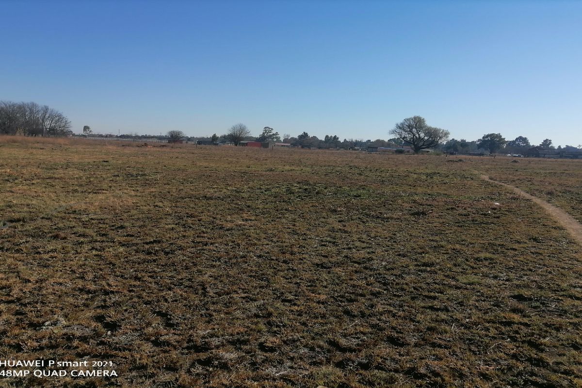 A wide-angle view of an expansive, undeveloped plot of land with dry grass and distant trees under a clear blue sky.