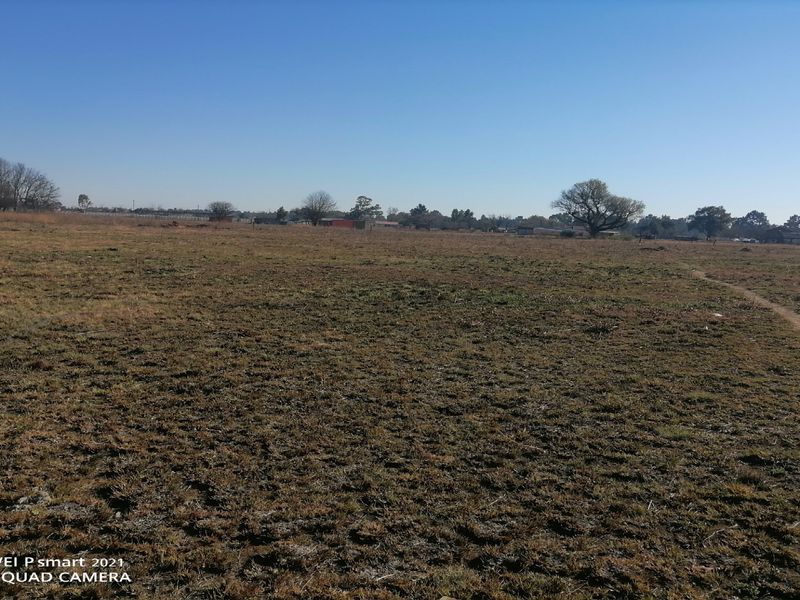A wide-angle view of an expansive, undeveloped plot of land with dry grass and distant trees under a clear blue sky.