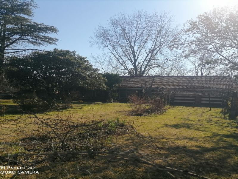 A view of the rear exterior of the property featuring a tiled roof building set within a large, overgrown garden area.