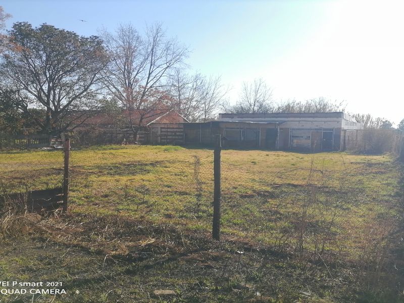 A view of the rear exterior of the property featuring a large open plot of land with wire fencing and a weathered single-story building.