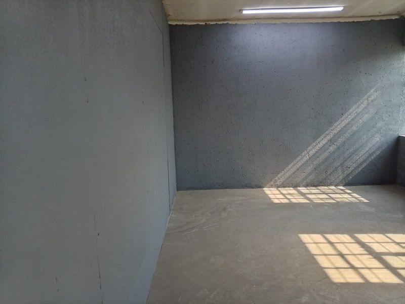 An empty industrial utility space featuring concrete flooring, textured grey walls, and overhead fluorescent lighting, suitable for storage or workshop use.