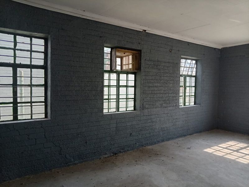 An empty industrial utility space featuring exposed painted brick walls, concrete flooring, and steel-framed windows with security bars.