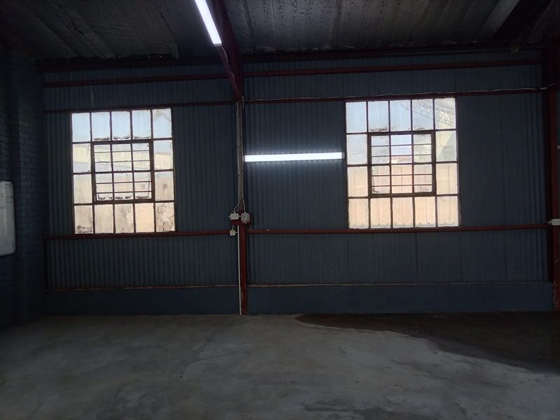 Spacious industrial utility area featuring corrugated metal walls, exposed steel beams, concrete flooring, and large industrial-style windows providing natural light.