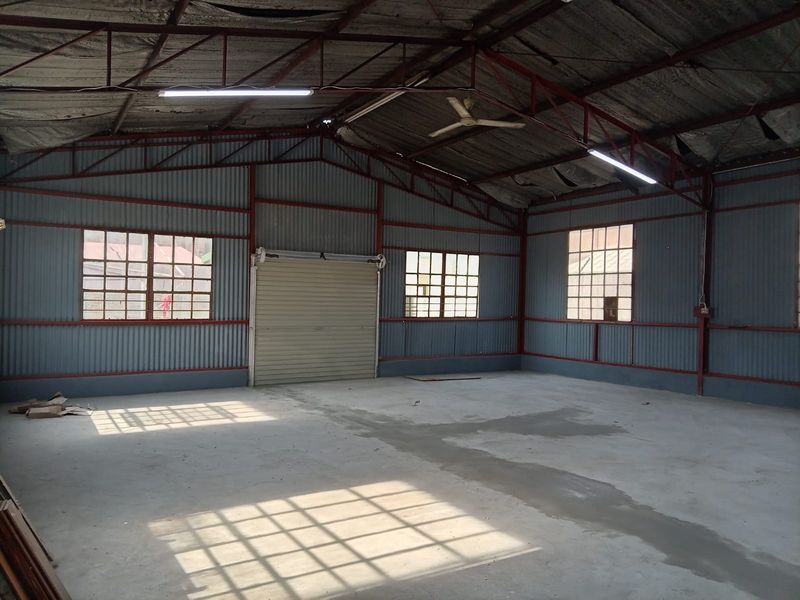 Spacious industrial utility space featuring corrugated metal walls, exposed steel roof trusses, concrete flooring, and a roller shutter door.