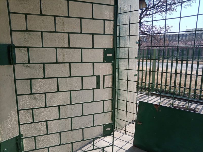 Exterior view of a secure industrial area featuring a metal security gate and fencing against a masonry wall.