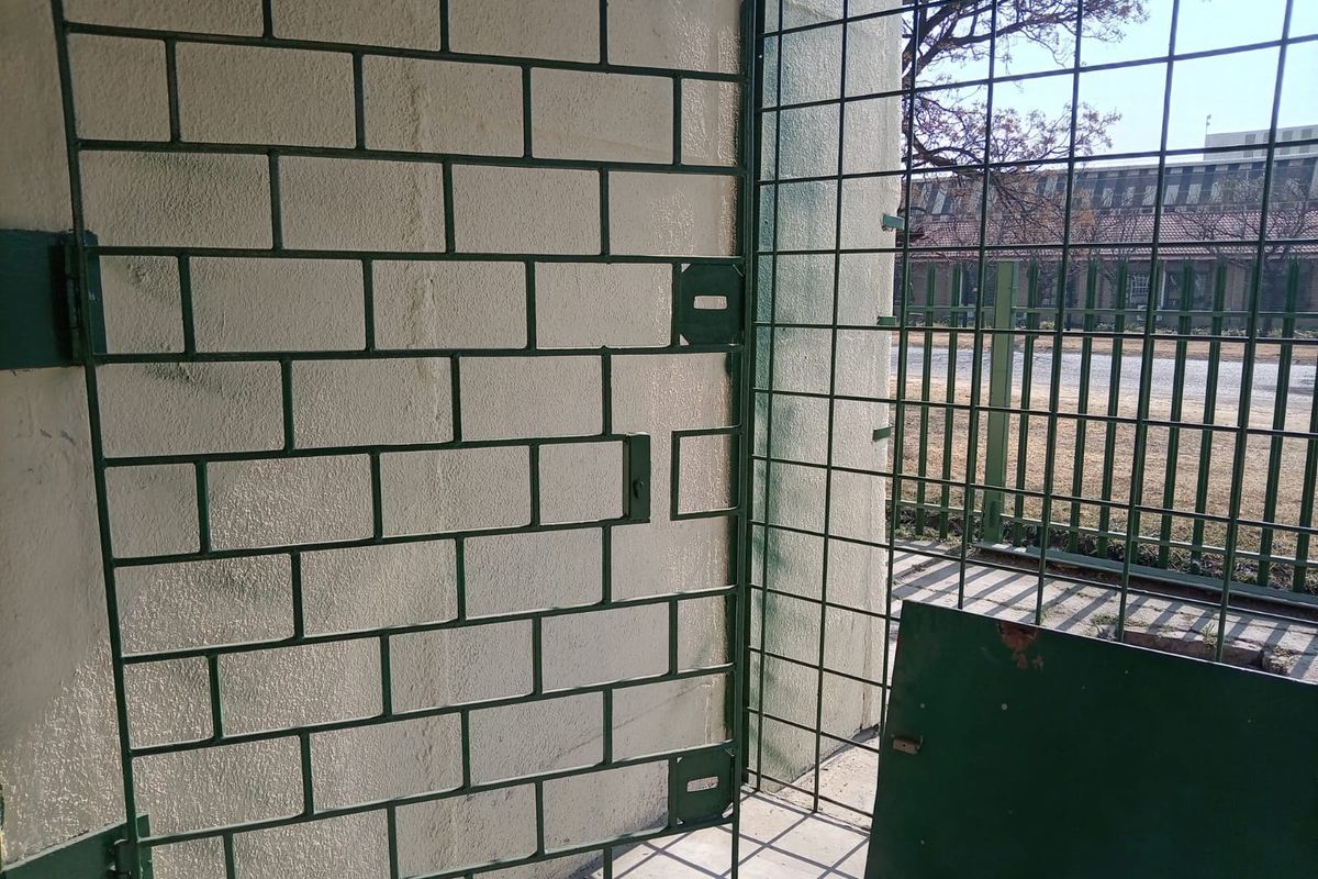 Exterior view of a secure industrial area featuring a metal security gate and fencing against a masonry wall.