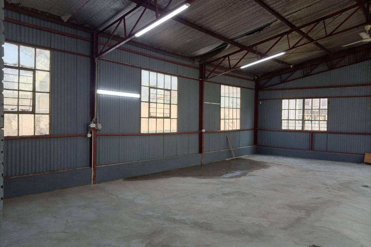 Spacious industrial utility area featuring corrugated metal walls, exposed steel roof trusses, concrete flooring, and ample natural light through grid-pattern windows.