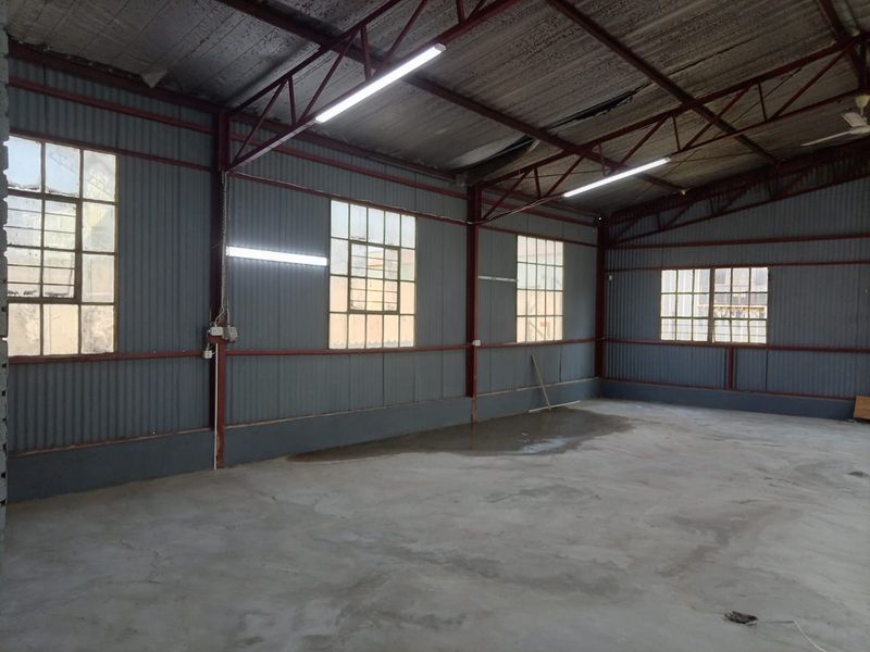 Spacious industrial utility area featuring corrugated metal walls, exposed steel roof trusses, concrete flooring, and ample natural light through grid-pattern windows.