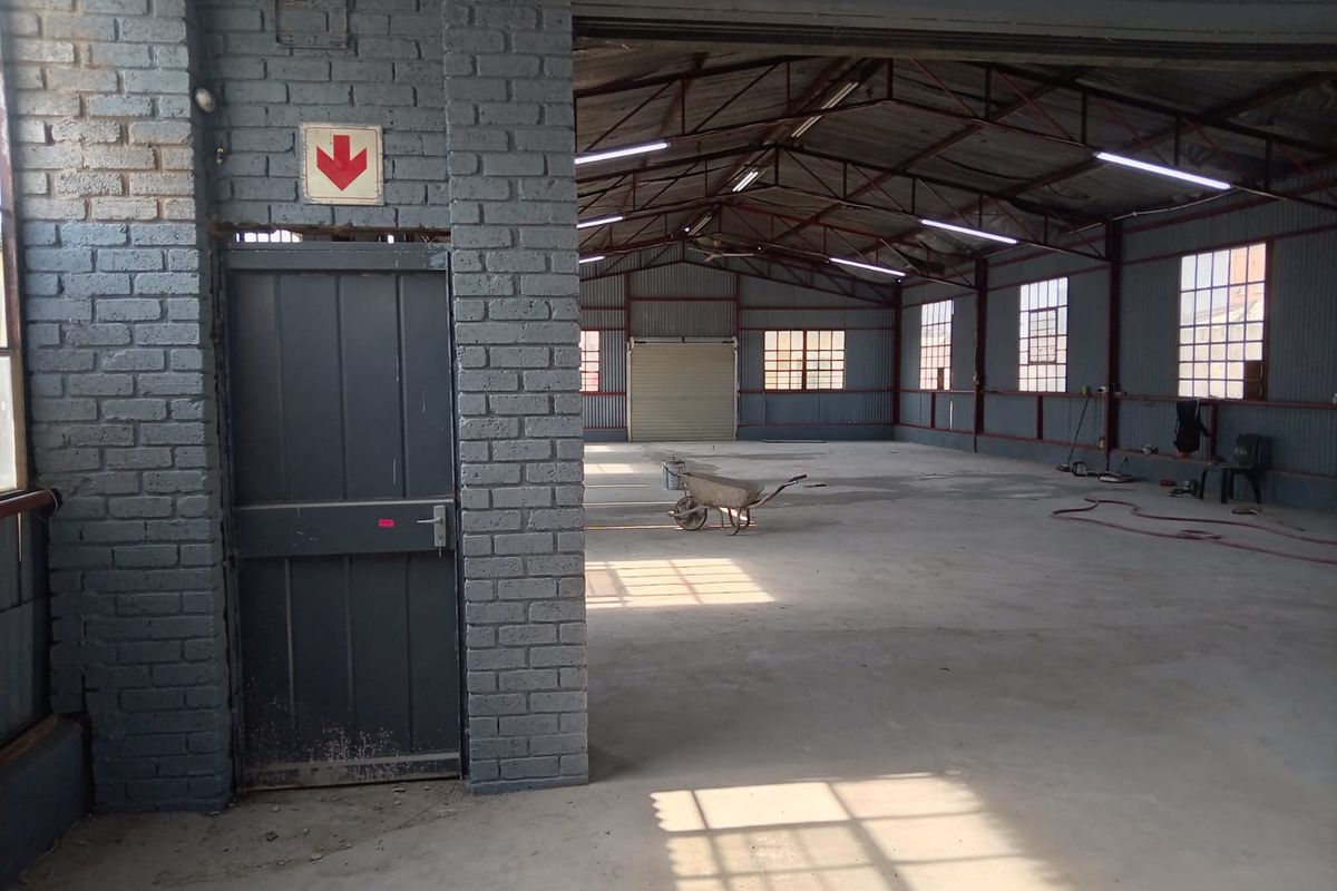 Spacious industrial utility area featuring exposed brick walls, steel roof trusses, concrete flooring, and a large roller shutter door for easy access.