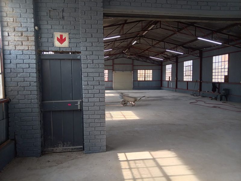 Spacious industrial utility area featuring exposed brick walls, steel roof trusses, concrete flooring, and a large roller shutter door for easy access.