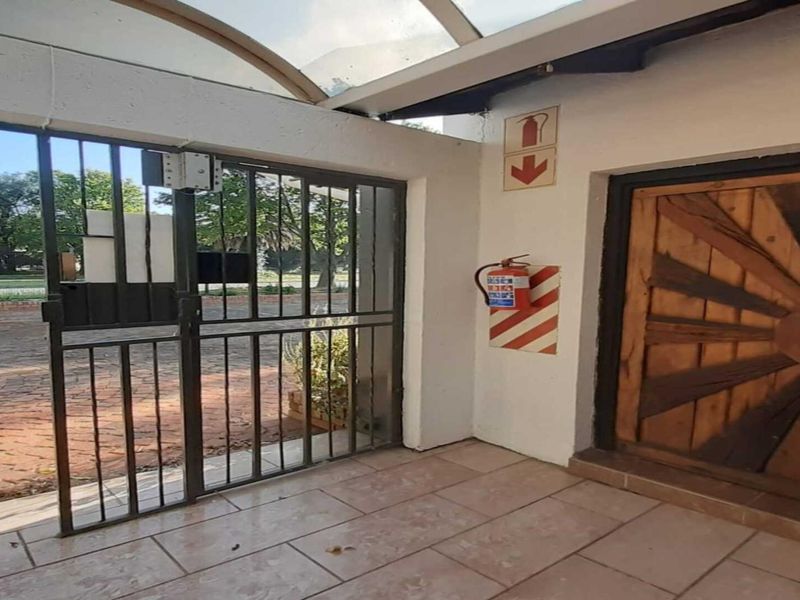 A covered entrance area featuring tiled flooring, a security gate, and essential fire safety equipment, providing access to the main office building.
