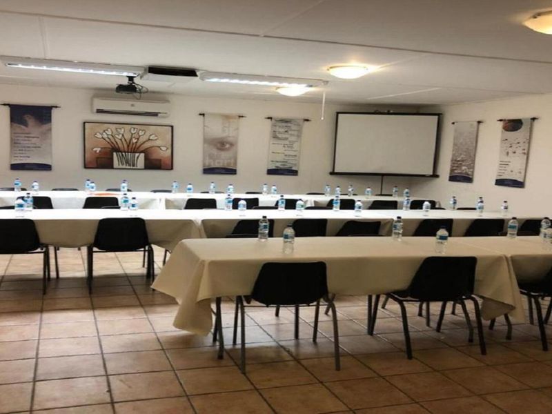 A functional office meeting room featuring tiled flooring, a drop ceiling with recessed lighting, a projector screen, and wall-mounted air conditioning.