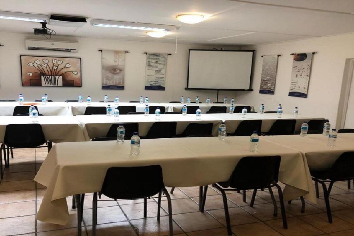 A functional office or meeting room space featuring tiled flooring, overhead lighting, and a wall-mounted projector screen for presentations.