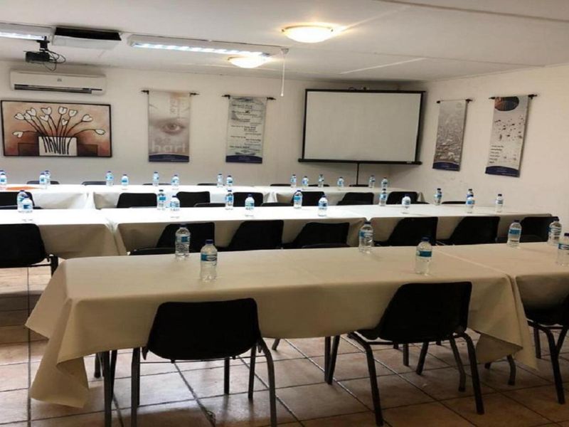 A functional office or meeting room space featuring tiled flooring, overhead lighting, and a wall-mounted projector screen for presentations.