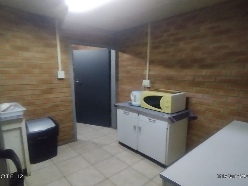 A functional office kitchenette featuring exposed brick walls, tiled flooring, and basic base cabinetry with a countertop.