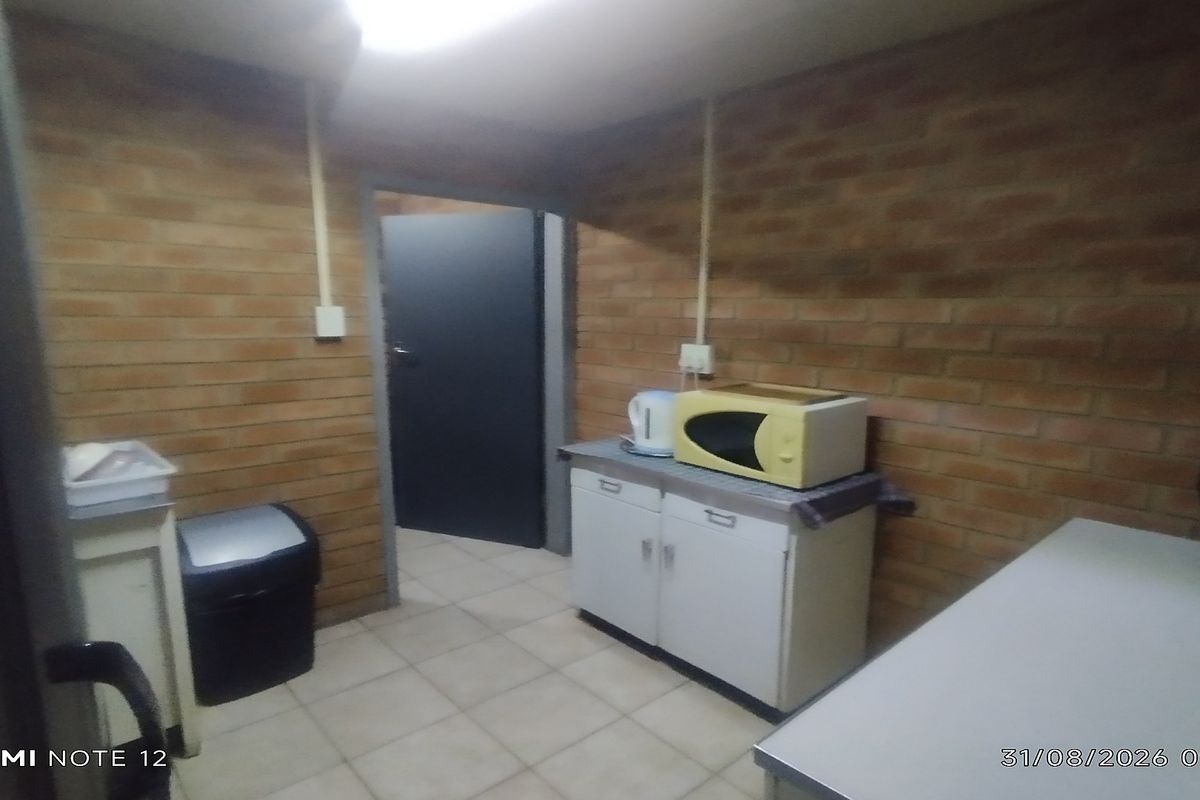 A functional office kitchenette featuring exposed brick walls, tiled flooring, and basic base cabinetry with a countertop.