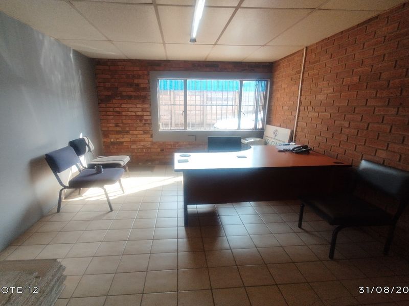 A functional office space featuring exposed brick walls, tiled flooring, and a suspended ceiling with integrated lighting.