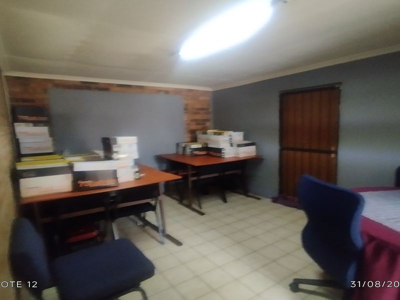 A functional office space featuring exposed brick wall accents, tiled flooring, and overhead fluorescent lighting.