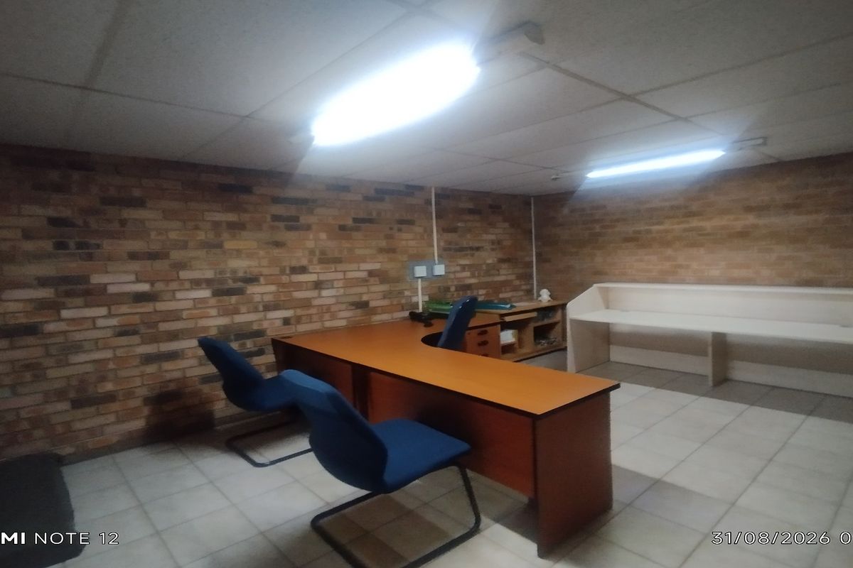 A functional office space featuring exposed brick walls, tiled flooring, and built-in desk cabinetry with overhead fluorescent lighting.