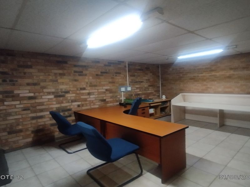 A functional office space featuring exposed brick walls, tiled flooring, and built-in desk cabinetry with overhead fluorescent lighting.