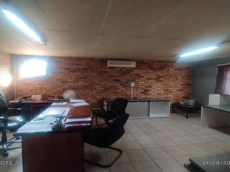 A functional office space featuring exposed brick walls, tiled flooring, suspended ceiling, and integrated air conditioning with built-in storage cabinetry.