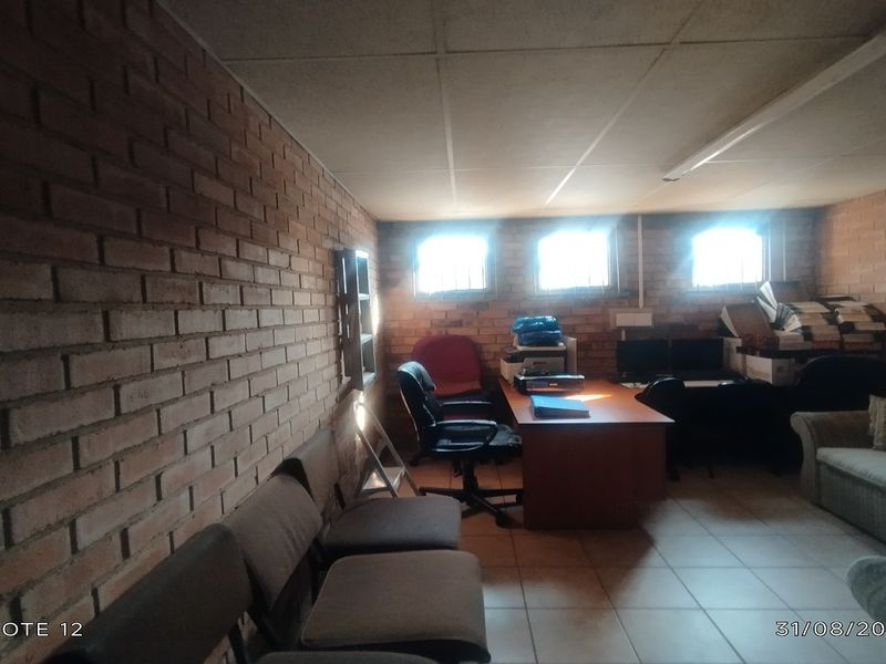 A functional office space featuring exposed brick walls, tiled flooring, and security-barred windows, providing a practical work environment with basic infrastructure.