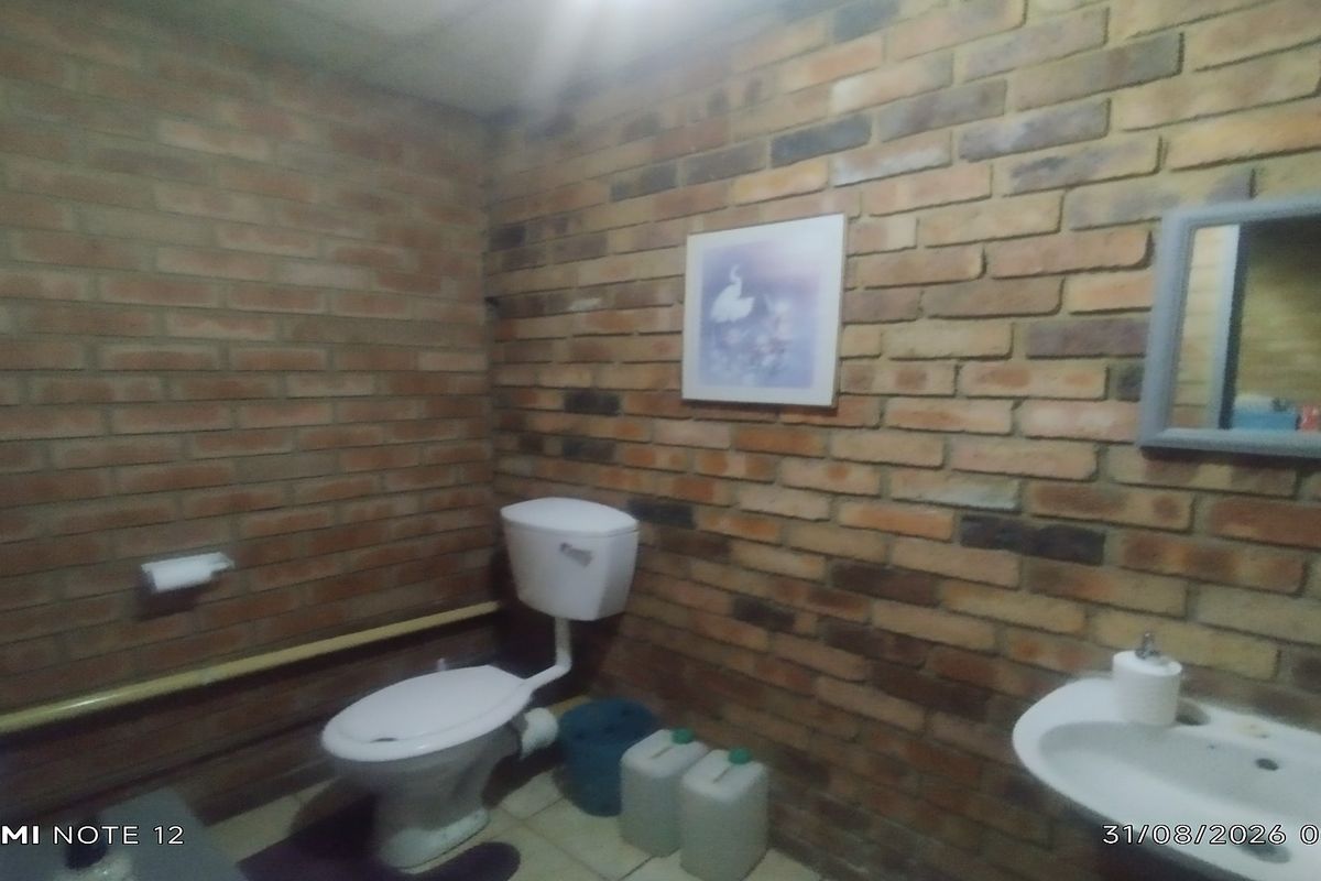 A functional bathroom featuring exposed brick walls, a standard toilet, and a wall-mounted basin with a grab rail.