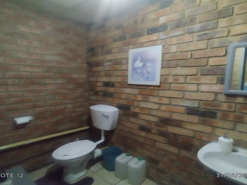 A functional bathroom featuring exposed brick walls, a standard toilet, and a wall-mounted basin with a grab rail.