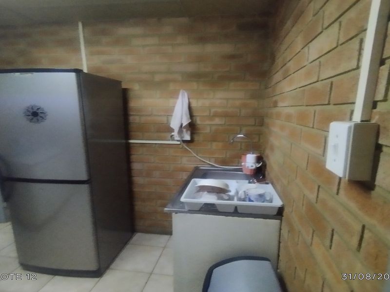 A small kitchenette area featuring exposed brick walls, tiled flooring, and a basic stainless steel sink unit with surface-mounted electrical infrastructure.