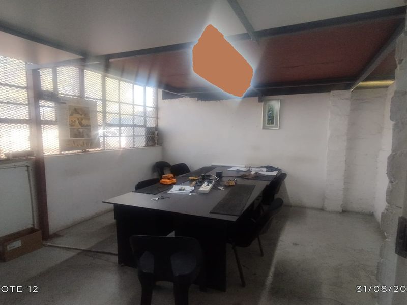 A functional office space featuring industrial-style steel-framed windows, exposed ceiling beams, and concrete flooring, suitable for commercial use.