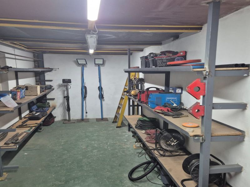 A functional utility or storage space featuring industrial metal shelving, exposed ceiling joists, and painted concrete flooring, suitable for workshop or storage use.