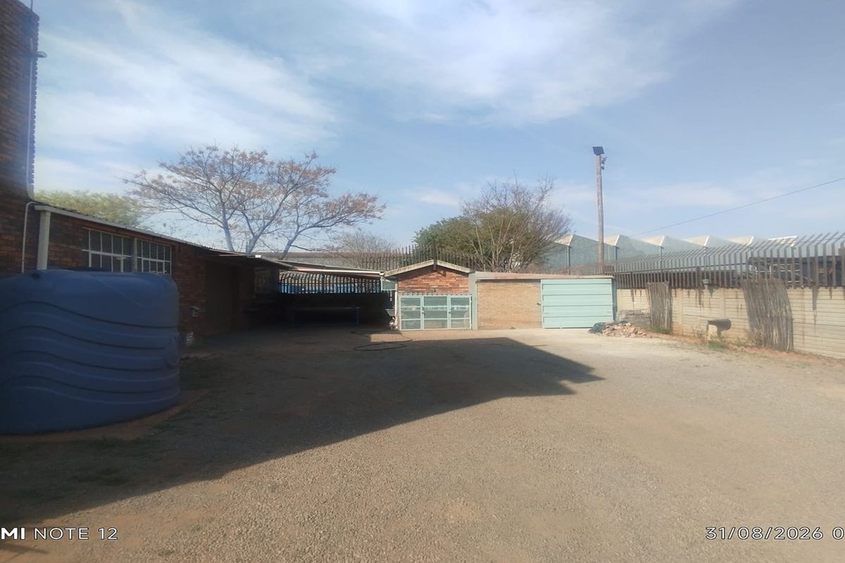 Rear exterior yard area featuring a gravel surface, water storage tank, and secure perimeter walling with metal fencing.