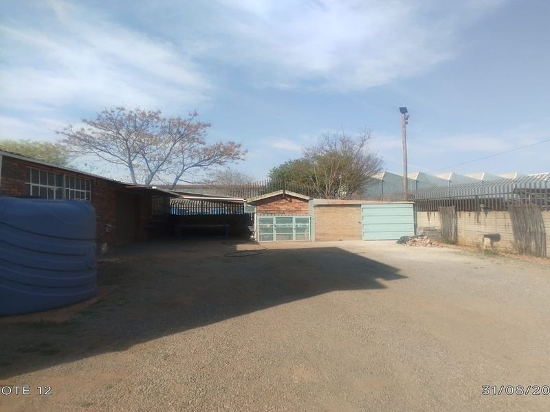 Rear exterior yard area featuring a gravel surface, water storage tank, and secure perimeter walling with metal fencing.