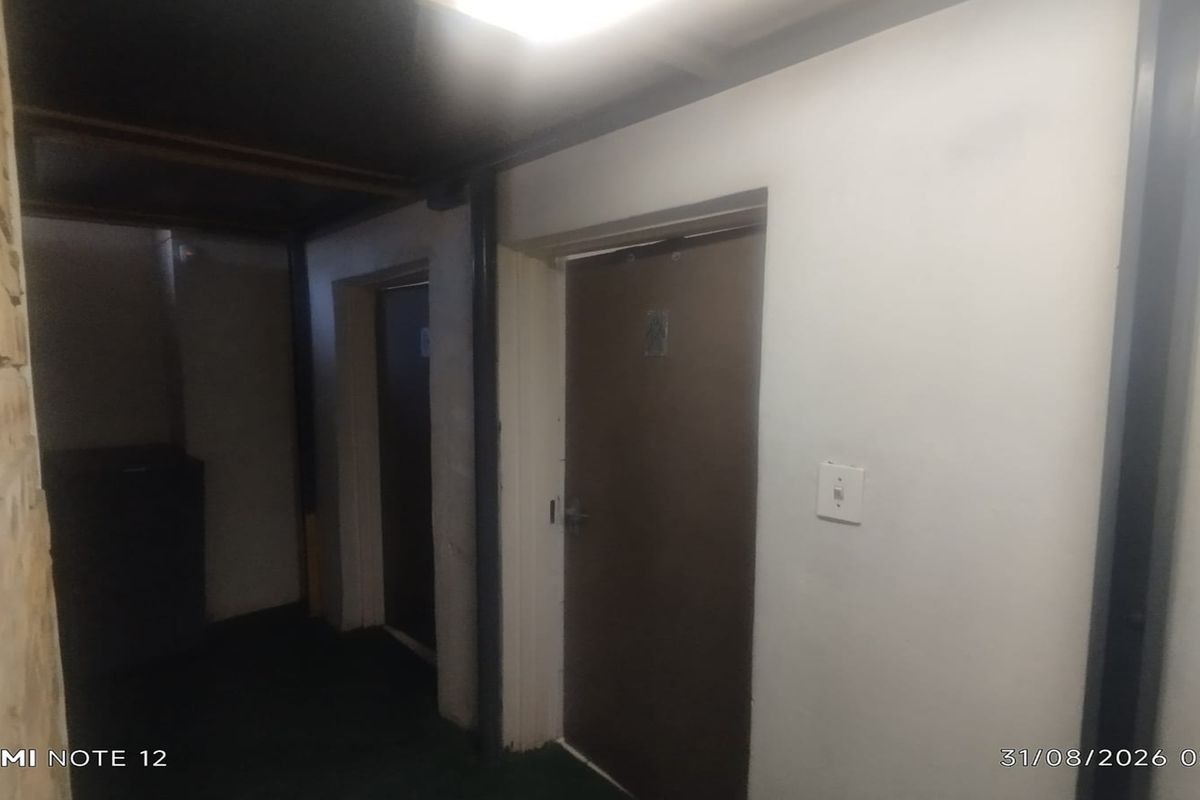 A dimly lit commercial hallway featuring multiple internal doors and exposed brickwork, requiring cosmetic updates to improve the overall aesthetic and brightness.
