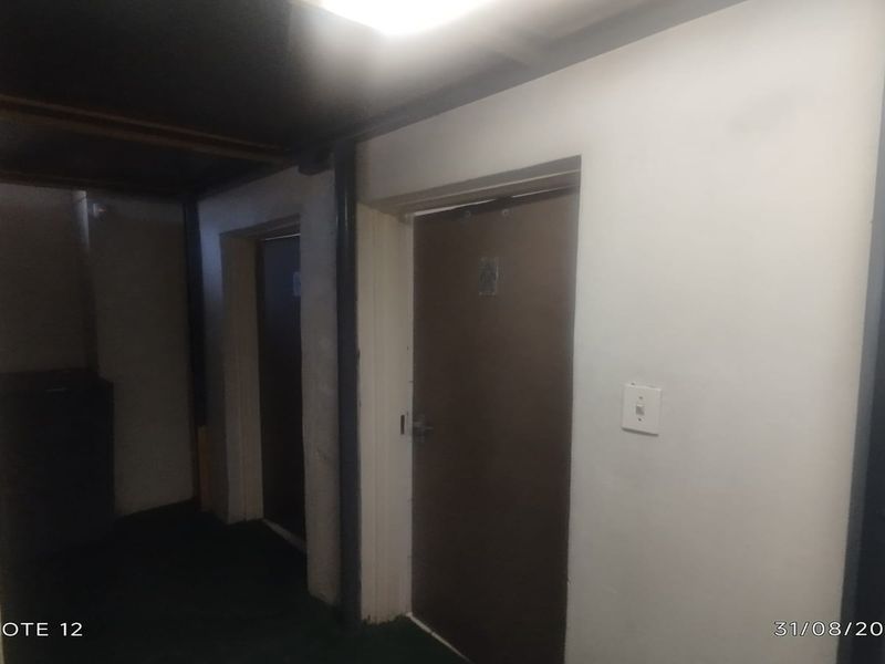 A dimly lit commercial hallway featuring multiple internal doors and exposed brickwork, requiring cosmetic updates to improve the overall aesthetic and brightness.
