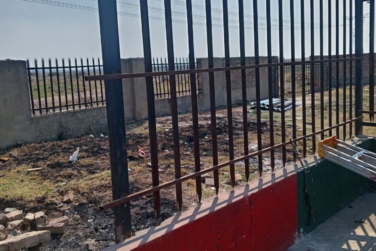 View of the industrial property's rear perimeter, featuring a metal spike fence on a concrete base with signs of wear and surface corrosion.