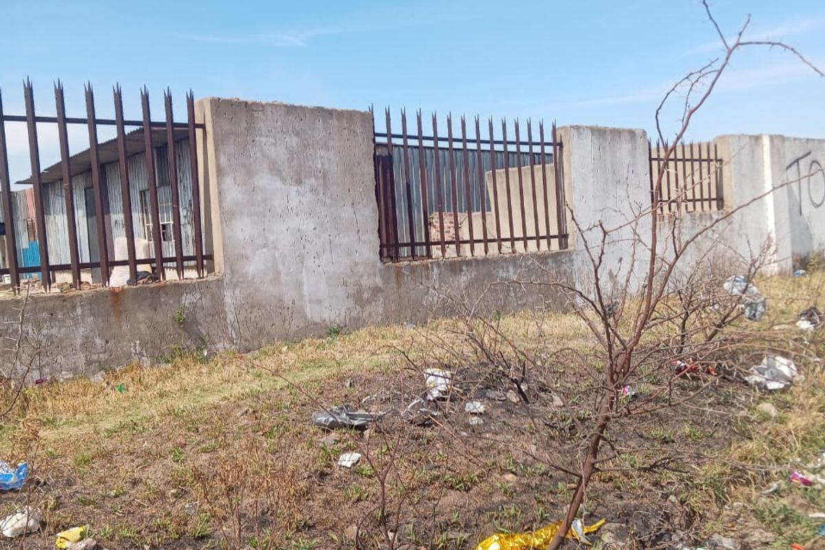 Exterior view of an industrial property boundary featuring a concrete wall with metal security fencing and spikes.