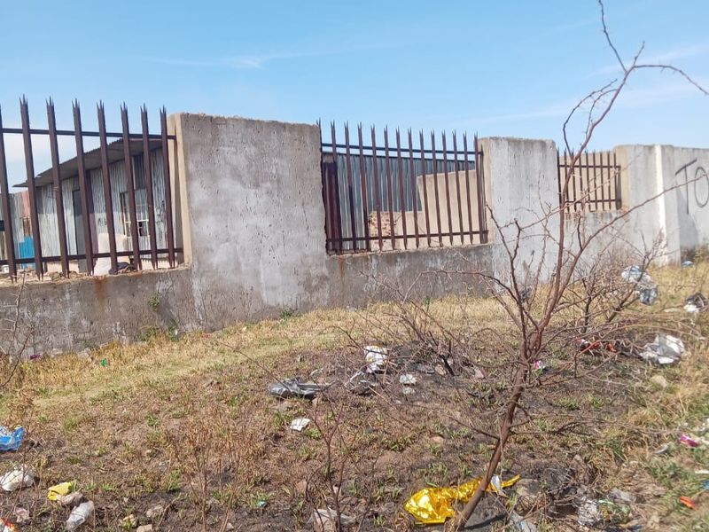 Exterior view of an industrial property boundary featuring a concrete wall with metal security fencing and spikes.